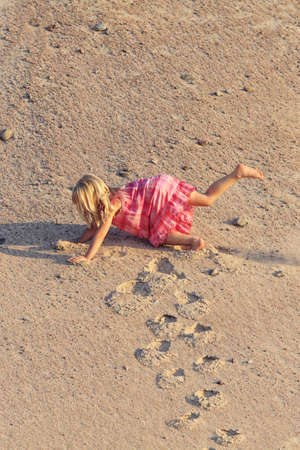 Funny girl falls in red dress from the mountain of sandの写真素材