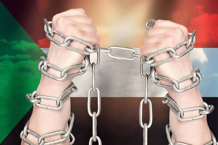 Two hands shackled a metal chain  of the Sudan flag. Freedom conceptの写真素材