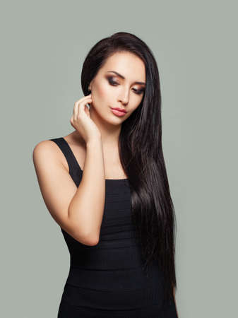 Pretty model woman with long straight hair and makeup wearing black dress posing against gray wallの写真素材