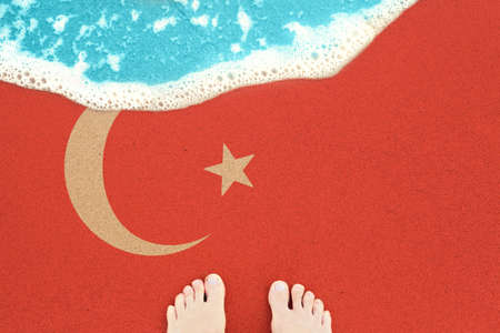 Two feet on the sunny sandy beach with flag Turkey. View from top on surf.の写真素材