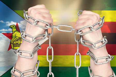 Two hands shackled a metal chain on Zimbabwe flag. Freedom conceptの写真素材