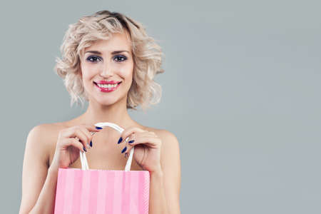 Happy blonde woman holding pink shopping bags and smilingの写真素材