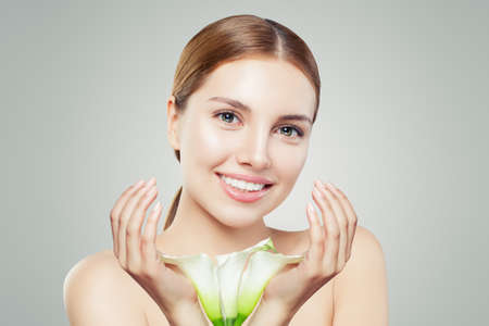 Beautiful young woman with clear skin and flowers on gray backgroundの写真素材