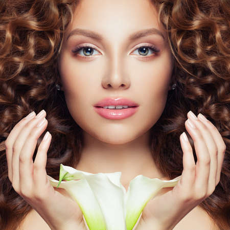 Pretty face. Perfect model woman with curly hair, clear skin and flowerの写真素材