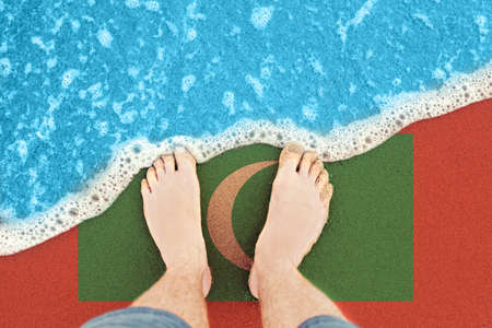Two Feet on sandy beach with flag Maldives. Top View on surf.の写真素材