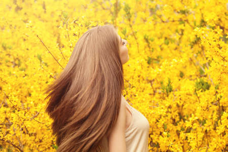 Beautiful young woman with long healthy hair against yellow flowersの写真素材