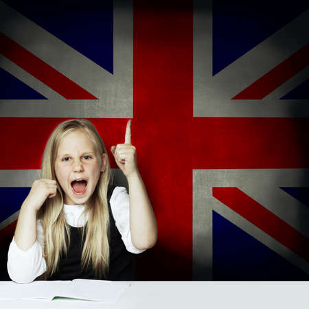 Happy child girl student pointing up and having fun against the UK flagの写真素材