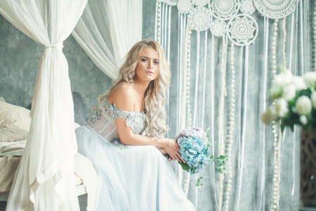 Beautiful blonde woman with flowers relaxing in vintage interiorの写真素材