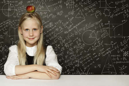 Cute child student girl with red apple on head. Blackboard background with science formulas....