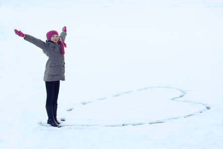 Pretty girl In The Winter Clothes Drawing Heart On Snow. Trace on snowの写真素材