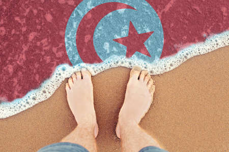 Two feet on beach with flag Tunisia. Top View on sea wave.の写真素材
