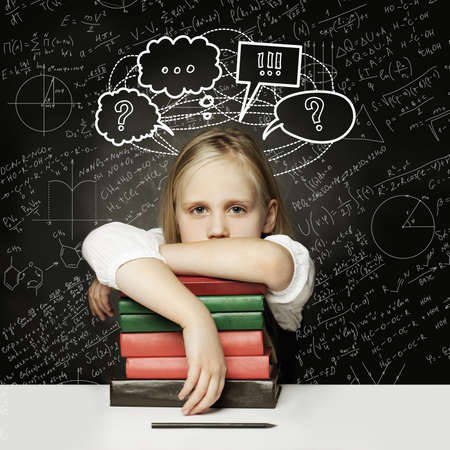 Tired child with books. little student thinking with thumb up and empty speech clouds bubbles on chalkboardの写真素材