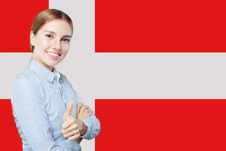 Travel and learn danish language concept. Happy Smiling woman student showing thumb up against the Denmark flag backgroundの写真素材