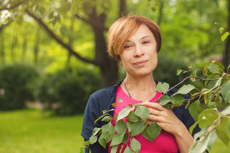 Beautiful older woman with green leaves outdoor. Pretty mature model 60 years oldの写真素材