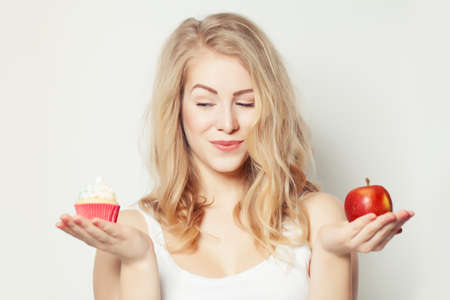 Smiling Beautiful Woman with crafty look. Healthy and Unhealthy Food. Difficult choice. Overweight Conceptの写真素材