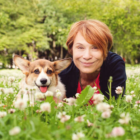 Senior woman with her pet friend dog on green grass in summer park portraitの写真素材