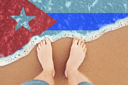 Feet on sandy beach with flag Cuba. Top View on sea surf.の写真素材