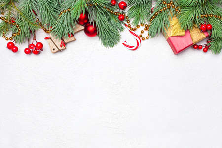 Christmas border composition with green Xmas fir branch, red holly berries and baubles on white texture stucco plaster background. Flat lay, top view with copy spaceの写真素材