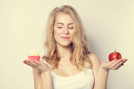 Smiling Beautiful Woman with crafty look. Difficult choice between Healthy and Unhealthy Food. Overweight Conceptの写真素材