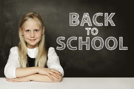 Smiling blonde child girl thinking on chalkboard. Back to school backgroundの写真素材