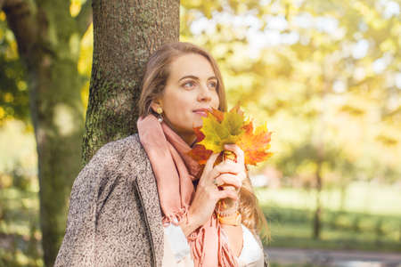 Beautiful woman holding yellow maple leaf outdoors. Romantic girl dreams in autumn fall parkの写真素材