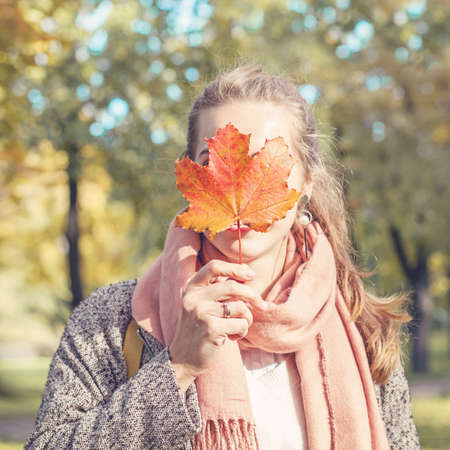 Beautiful autumn woman holding yellow maple leaf. Romantic girl in fall parkの写真素材
