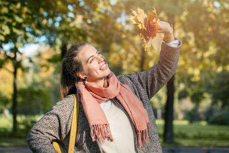 Beautiful autumn woman looking at sun through yellow maple leaf outdoors. Romantic girl in fall parkの写真素材