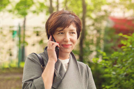 Pretty mature woman phone, outdoors portraitの写真素材