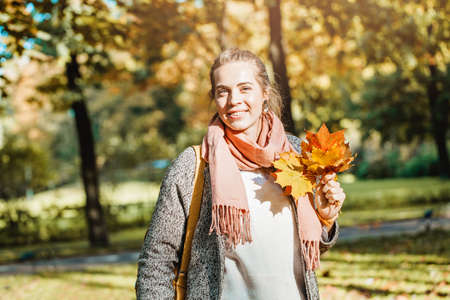 Beautiful smiling woman holding autumn yellow maple leaf outdoors. Romantic girl in fall parkの写真素材