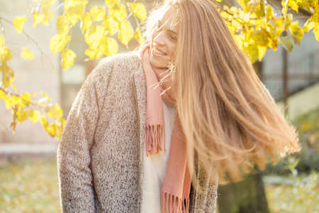 Beautiful autumn woman holding yellow maple leaf outdoors. Romantic girl with long hair in fall parkの写真素材