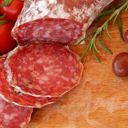 Gourmet food - salami, olives and rosemary herbs on wooden tableの写真素材
