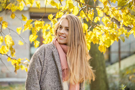 Cute autumn woman holding yellow maple leaf outdoors. Romantic girl with long hair in fall parkの写真素材