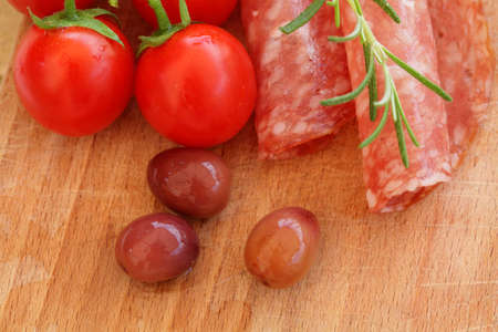 Gourmet food - salami, olives, tomatos and rosemary herbs closeup on wooden tableの写真素材