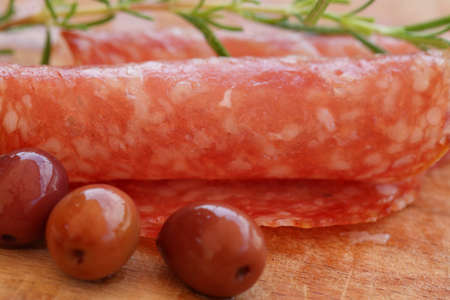Gourmet food - salami, olives and rosemary herbs closeup on wooden tableの写真素材