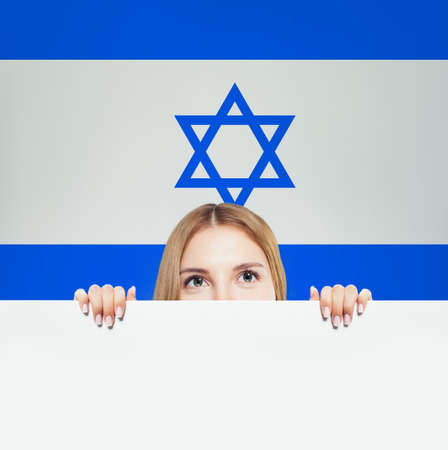 Beautiful happy young woman showing white paper against the Israel flagの写真素材