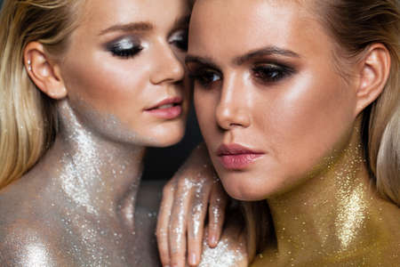 Fashion portrait of pretty women with gold and silver glitter makeup, face closeupの写真素材