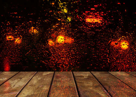 Rain drops on glass surface with red bokeh night city lights with wooden table