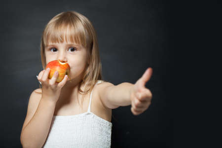 Kid eating fresh red apple happy and doing ok sign, thumb up with fingers, excellent signの写真素材