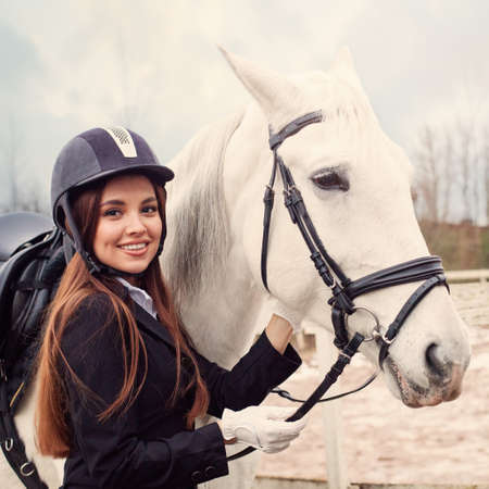 Vintage fashion portrait of beautiful jockey woman and white horseの写真素材