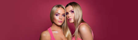 Two pretty young women with makeup and long blonde hair on pink banner background with copy spaceの写真素材