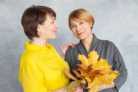 Autumn portrait of two mature women with fall maple leavesの写真素材