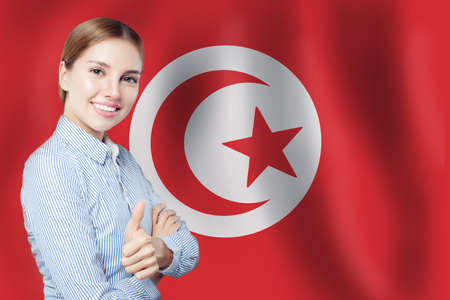 Portrait of happy smiling woman with thumb up on Tunisia flag background. Travel in Tunisiaの写真素材