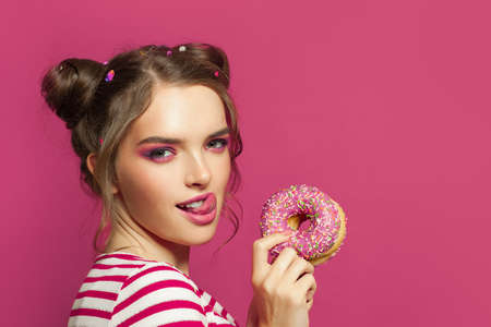 Pretty woman with donut and tongue lick one's lips on colorful pink backgroundの写真素材