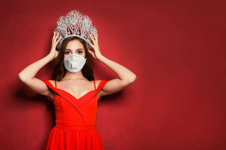 Fashion woman in medical face mask and diamond crown on red backgroundの写真素材