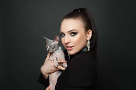 Glamorous woman in diamond earrings with sphynx cat on black backgroundの写真素材