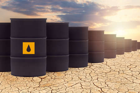 Black oil barrels against sky clouds and dried depleted land