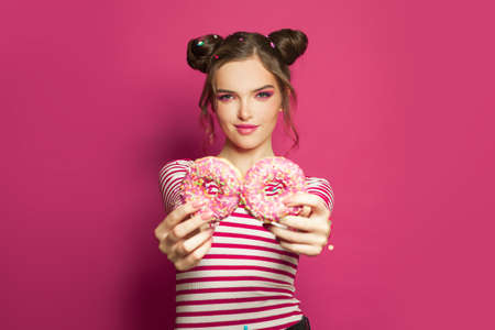 Smiling young woman with donuts on pink backgroundの写真素材