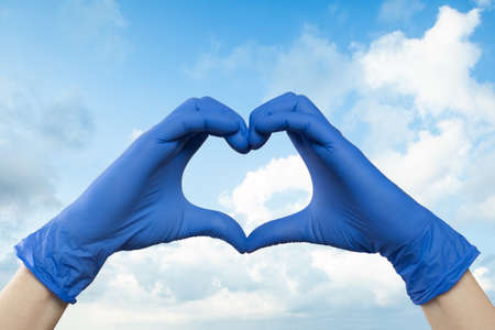 Doctor hands showing heart against sky cloudsの写真素材