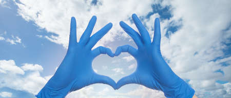 Doctor hands making heart against sky clouds backgroundの写真素材