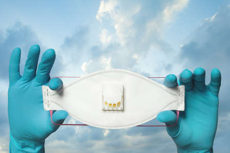 Hands in doctor gloves showing protective mask against sky clouds background, safety and virus...